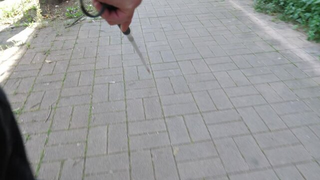 A point of view shot of a blind man walking with a cane. The scene captures his perspective and the experience of navigating the environment.