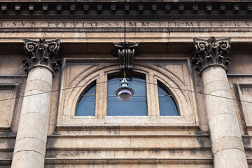 A street lamp hanging on wires against the backdrop of a building facade with columns and a large thermal window.
