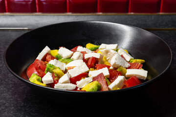 Fresh red tomato, avocado and bryndza or feta salad with olive oil in black dish close-up side view, healthy eating.