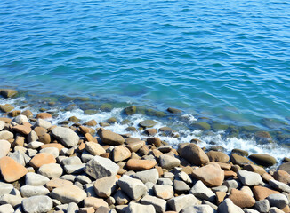 Calm azure water gently lapping against a rocky shoreline under clear skies in a serene coastal setting