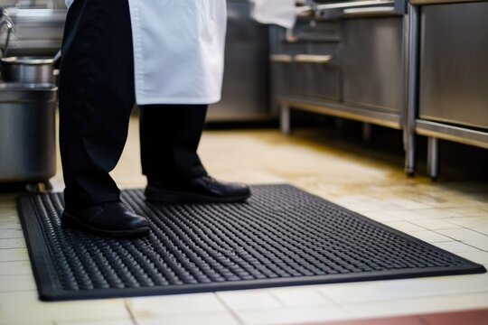 A chef standing on a mat in a kitchen preparing food