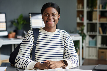 Portrait of smiling African American woman sitting at office desk with a relaxed and confident expression, featuring organized workspace background, reflecting work environment