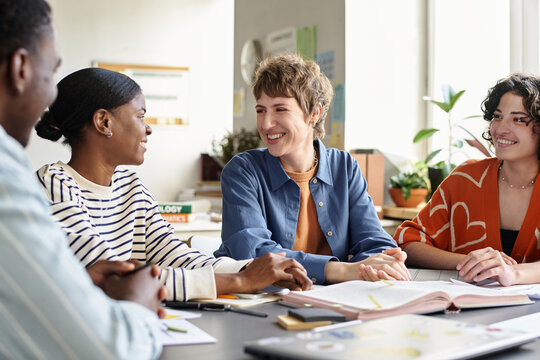 Diverse group of colleagues collaborating on project ideas in contemporary office space, maintaining positive interaction and engagement. Several documents and notebooks spread on the table