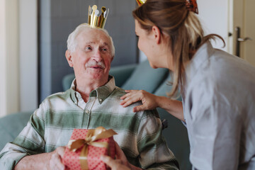 Smiling healthcare worker with man holding gift and celebrating birthday at home
