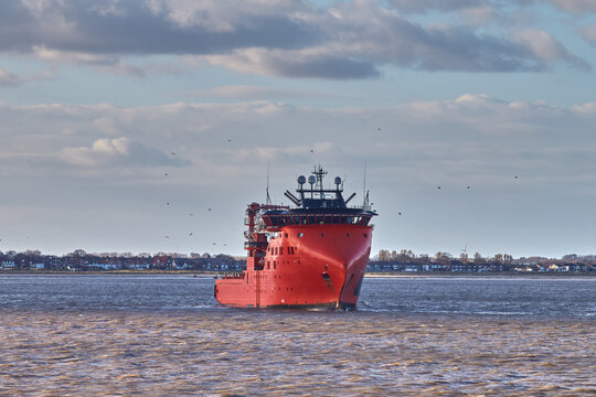 Red offshore support vessel navigating in port.