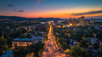 Obraz premium A stunning aerial view of a cityscape at dusk, showcasing the vibrant glow of streetlights and illuminated buildings against a backdrop of a breathtaking sunset.