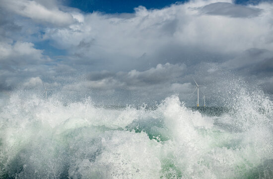 Water splashing in sea with wind farm under cloudy sky