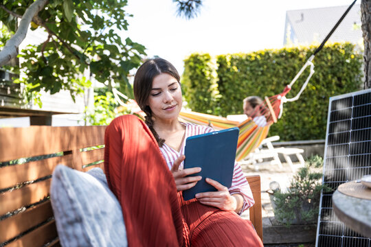 Smiling young woman using tablet PC on bench in back yard