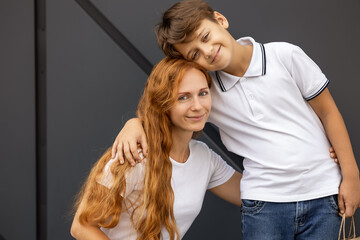woman with long red hair smiles tenderly as she kneels next to her little son who wears white polo...