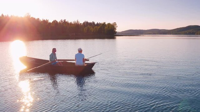 Aerial shot of an older couple rowing and fishing on a romantic sunset lake