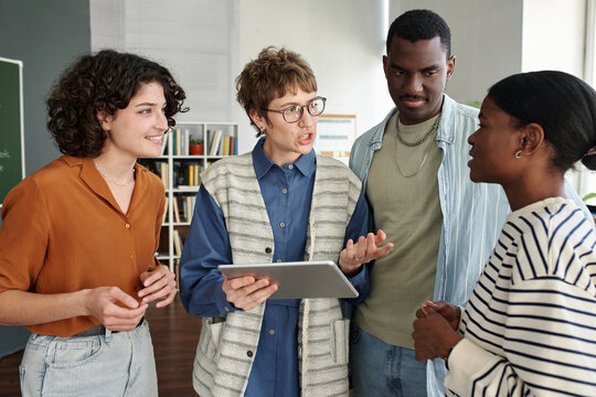 Group of four people engaging in conversation while one holds a tablet. They are participating in a collaborative discussion in an academic setting