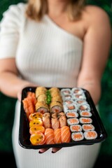 Sushi platter held by woman in white dress.