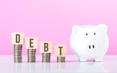 A Stack of coins atop a wooden block labeled 'DEBT' beside a white piggy bank. Represents financial...