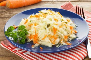 Coleslaw salad with carrots and parsley on blue plate with napkin and fork on rustic table