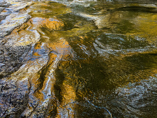 close-up abstract photo of a water surface with sunlight reflecting off the rippling water. natural pattern of gold, blue