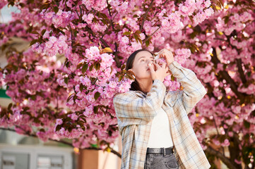 Woman allergic using medical eyes drops, suffering from seasonal allergy at spring in blossoming...