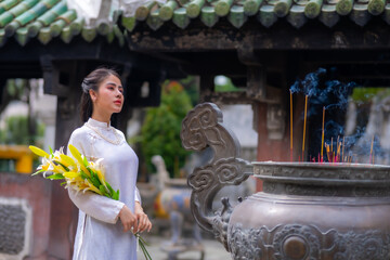 Vietnamese girl with Ao Dai dress standing in temple in Ho Chi Minh city, Vietnam. Ao dai is famous...
