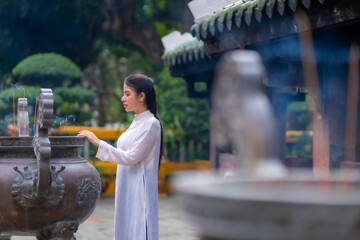 Vietnamese girl with Ao Dai dress standing in temple in Ho Chi Minh city, Vietnam. Ao dai is famous...
