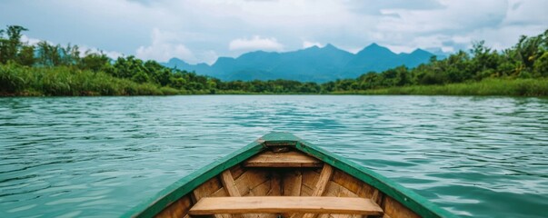 Naklejka premium Serene view from a boat on a tranquil lake, surrounded by lush greenery and mountains under a cloudy sky.