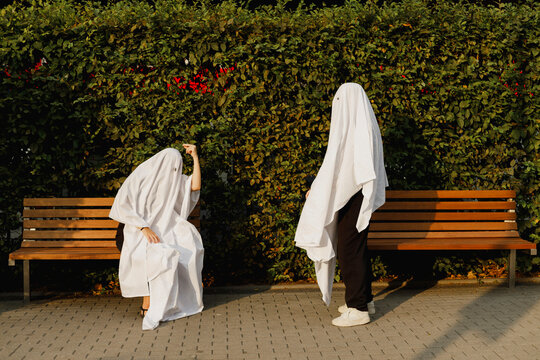 Couple wearing ghost costumes and taking to each other near plants