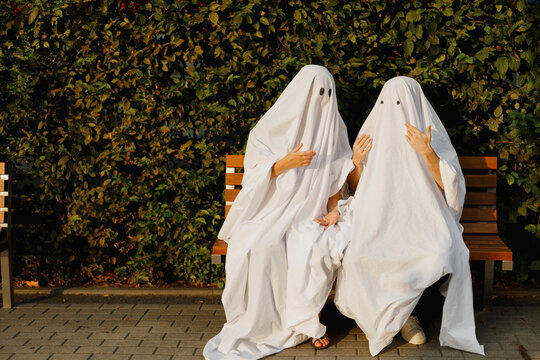 Young couple wearing ghost costumes and talking to each other on bench