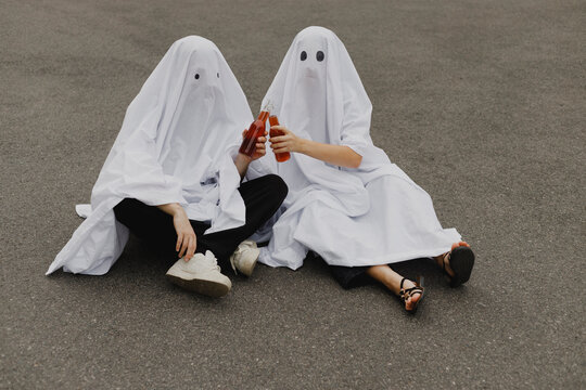 Couple wearing ghost costumes and toasting glass beer bottles on road