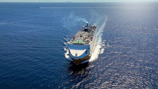 Panoramic aerial view of a large, industrial car carrier transport ship cruising with speed over the ocean