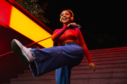 Happy woman with smart phone listening music on headphones and dancing at night