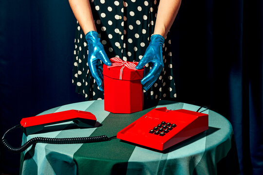 Woman opening Christmas present kept near old-fashioned telephone on table in studio