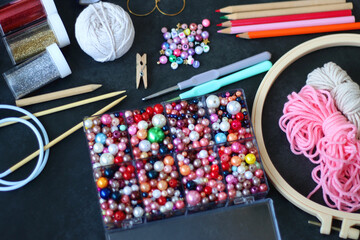 Colorful beads, coloring pencils, glitter, needles, string, hoop, tape and scissors on dark...