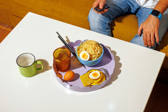 Mature man holding TV remote and having dinner at table on sofa