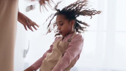 A young black woman dances joyfully inside a bright room filled with natural light. Her expressive movements highlight her enjoyment as she spins and explores her rhythm.