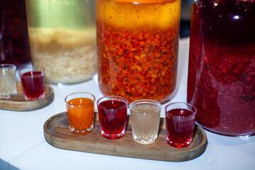 Enjoy tasting vibrant homemade fruit liqueurs on a rustic wooden tray. With red. Orange. And ginger flavors like sea buckthorn and raspberry. Savor unique shots of organic. Healthy beverages indoors