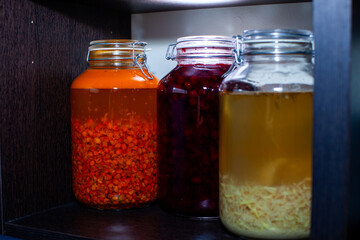 Glass jars filled with colorful homemade fruit and ginger preserves stand on a dark wooden shelf, showcasing the art of preserving nature's bounty