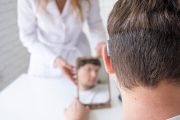 Fototapeta premium young male patient testing hearing aid in clinic exam room, female doctor helping