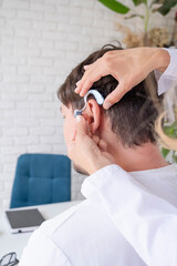 young male patient testing hearing aid in clinic exam room, female doctor helping