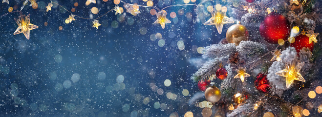 Christmas tree with Christmas balls on the background of the night sky - decorations on fir branches with shiny and unfocused lights and snowflakes on an abstract background