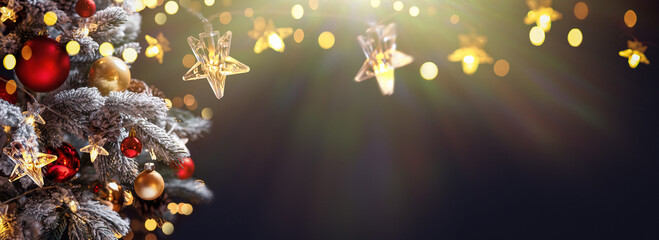 Christmas tree with Christmas balls on the background of the night sky - decorations on fir branches with shiny and unfocused lights and snowflakes on an abstract background