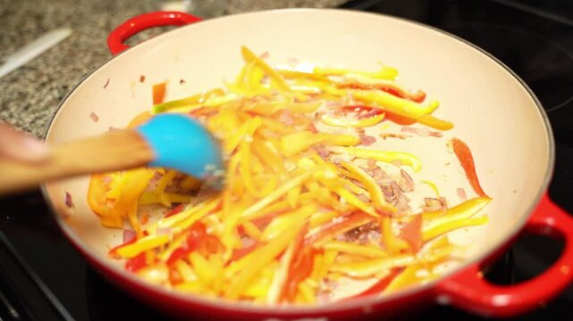 Stirring of veg cuisine having carrots, capsicums in frying pan.