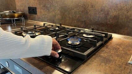 Woman's hand turns on a gas stove in a modern kitchen.