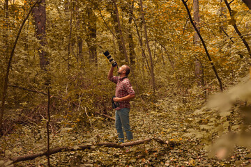 Man using binoculars and camera for bird and animal watching in nature.