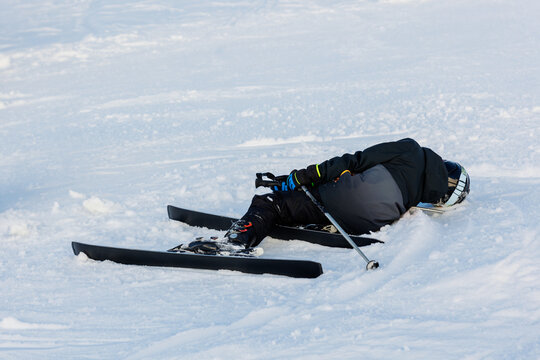 Little teen boy kid in black suit lying on snow after ski downhill accident crash. Tired beginner child learn skiing at winter ski camp school on mountain resort