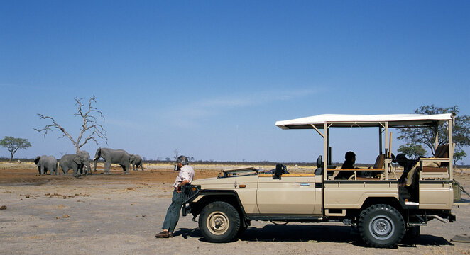Man leaning against a 4x4 drinking tea while observing  elephants, Botswana