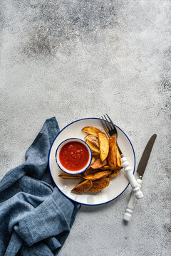 Overhead view of a plate of Fried potato wedges served with tomato sauce on a table