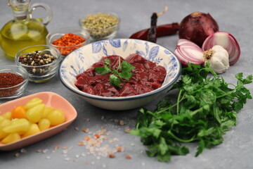 Cut raw beef liver with onions, spices, chili peppers and dill on wooden table, flat lay