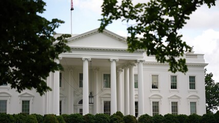 Closeup view through trees of the North side of the White House with fountain, green grass and flags flying in spring.