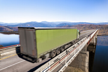 Green truck moving by a bridge over the river