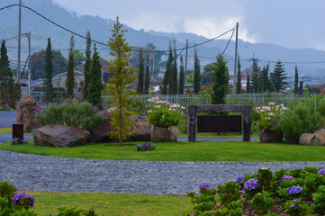 Naklejka premium A scenic mountain garden featuring large rocks and a winding pathway, surrounded by lush greenery and vibrant flowers. The overcast weather adds a serene ambiance.