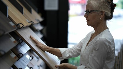 Closeup of happy mature woman running hand across solid or engineered wood plank samples in a floor or hardware store for a home remodeling renovation redecorating project.