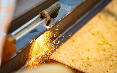 Skilled metalworker uses torch to cut through steel. Sparks fly as craftsman demonstrates precision in industrial workshop. Concept of balancing risk and expertise in dangerous metalworking processes.